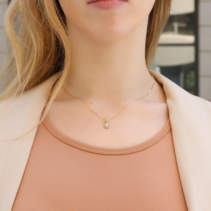 A drop-shaped halo pendant with a white opal stone on a 14K gold chain.